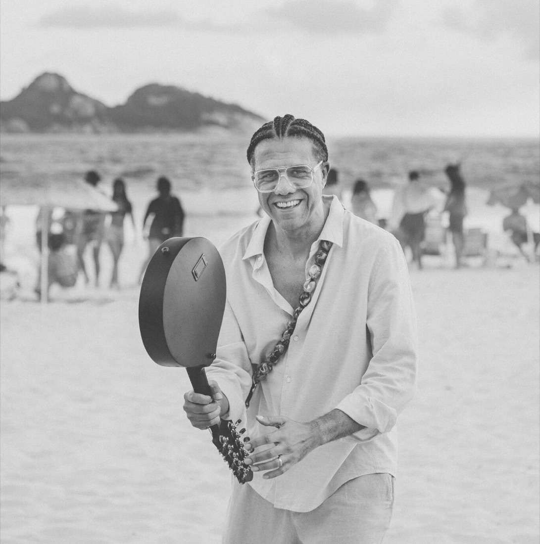 Hamilton de Holanda na praia, em preto e branco, sorrindo com o bandolim a tiracolo